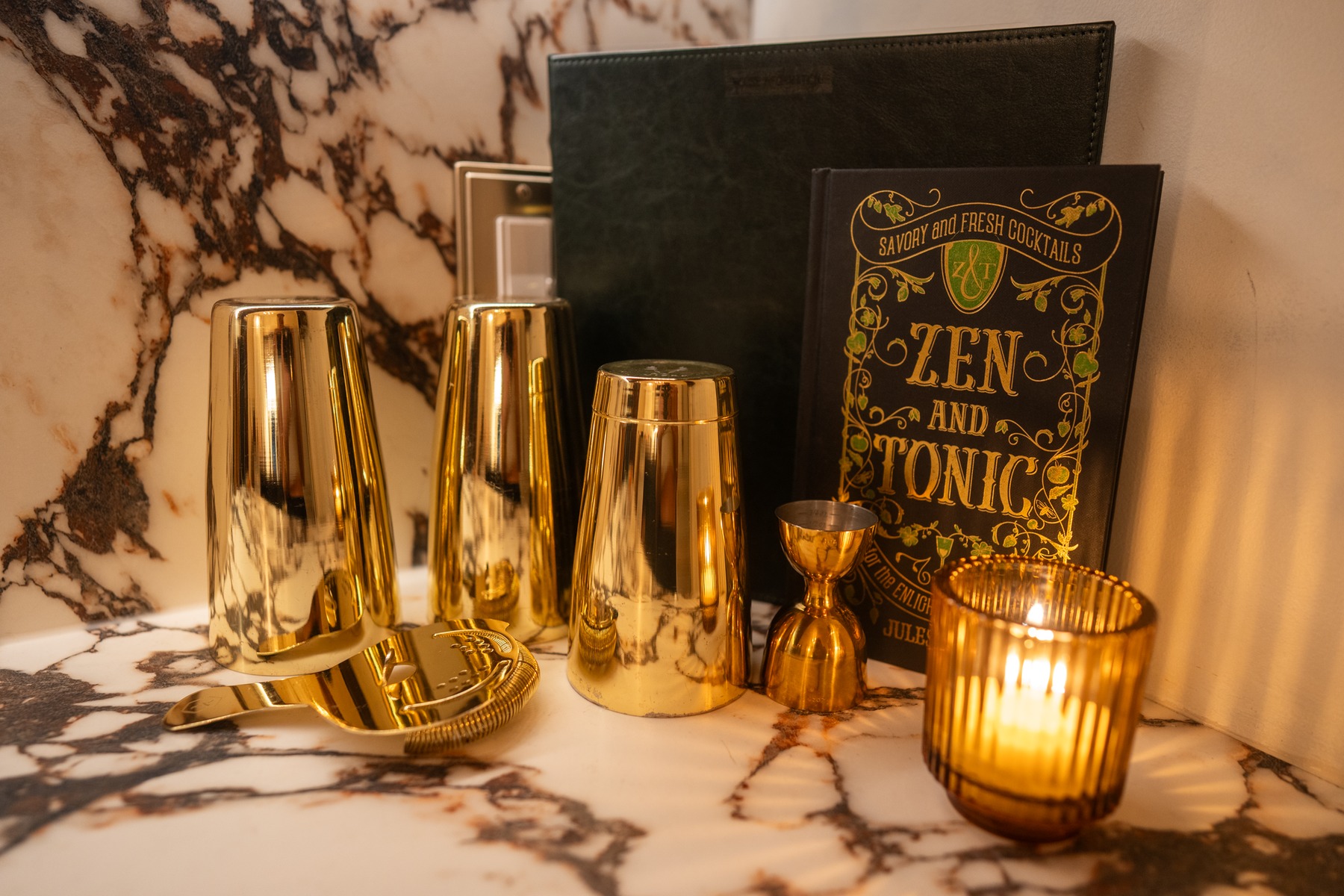 Gold cocktail shakers, jiggers, and a cocktail book on the bar